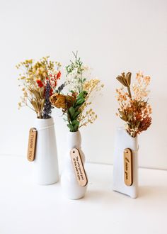 three white vases with flowers in them sitting on a counter top next to each other