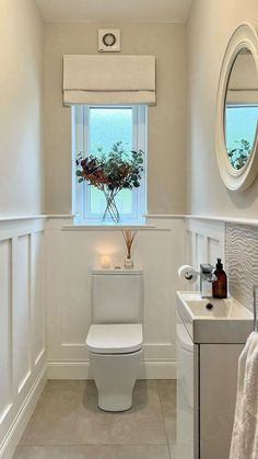 a white toilet sitting next to a sink in a bathroom under a window with a flower vase