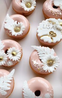 pink donuts decorated with white flowers and gold accents are on display in a box