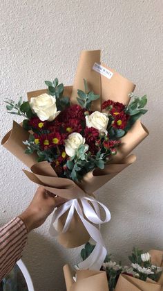 a person holding a bouquet of flowers in front of a white wall and brown paper bags