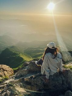 a woman sitting on top of a mountain looking at the sun