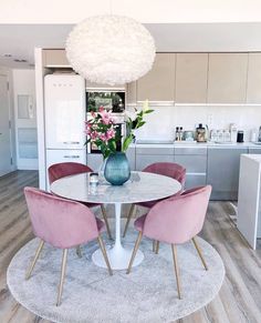 a white table with pink chairs and a blue vase on it in the middle of a kitchen