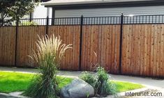 a wooden fence in front of a house with grass and rocks on the ground next to it