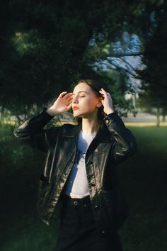 a woman in a black leather jacket and white shirt is holding her hands up to her ear