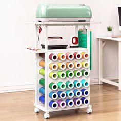 a white cart with lots of different colored spools on top of it and a computer desk in the background