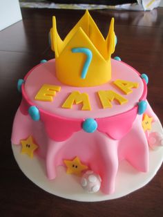 a pink cake with a yellow crown on top and stars around the edges that spell it's 7th birthday