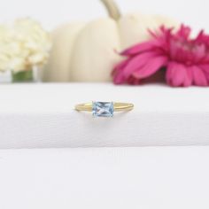 a ring with a blue topaz sits on a white surface next to flowers and a pumpkin