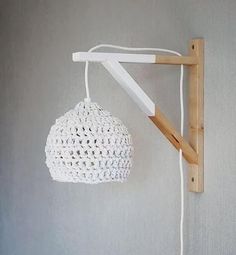 a white crocheted lamp hanging from a wooden frame on a wall next to a light fixture