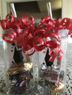 two mason jars filled with candy wrapped in red and gold paper streamers are sitting on a doily