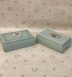 two small blue boxes sitting on top of a bed covered in hearts and flowers next to each other