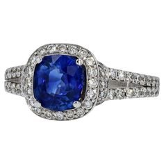 A contemporary sapphire and diamond engagement ring that commands attention. A 1.62 carat cushion cut sapphire is centered displaying a vibrant and deep blue. Accented by over 1 carat of shimmering, icy white diamonds forming the halo and open "V" split band. This design balances out the face of this gemstone engagement ring, spreading the treasured jewels around your finger. The 18 karat white gold band and setting pushes this ring over the top.   Condition: Very Good Era: Contemporary Year: 20 Sapphire And Diamond Engagement Ring, Gemstone Engagement Ring, Bleu Violet, Sapphire Engagement Ring, Gemstone Engagement, Split Shank, White Gold Band, Sapphire Engagement, Gemstone Engagement Rings