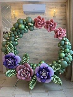 a wreath made out of balloons with flowers on the front and sides, sitting against a brick wall