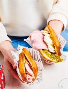 two people holding sandwiches with meat and cheese on them next to a can of soda