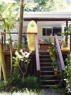 a surfboard sitting on top of a wooden deck next to trees and plants in front of a house