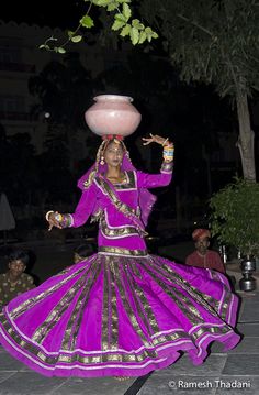 a woman dressed in purple dancing with a bowl on her head