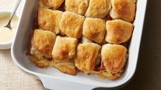 a casserole dish filled with meat, cheese and bread rolls next to a bowl of ranch dressing