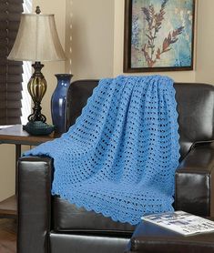 a blue crocheted blanket sitting on top of a black chair next to a lamp