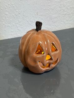 an orange pumpkin with glowing eyes on a gray counter top next to a white wall