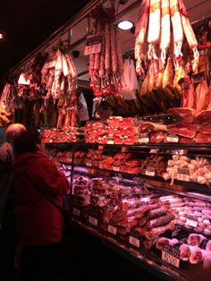 people looking at meat in a market with lights on and hanging from the ceiling above