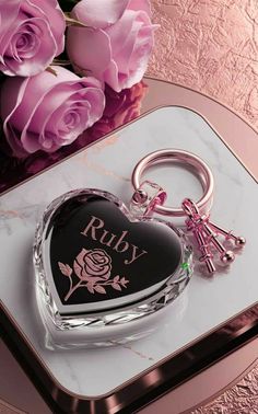 a heart shaped keychain sitting on top of a table next to pink roses