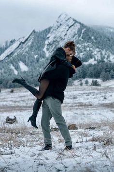 a man carrying a woman on his back while walking through the snow covered ground with mountains in the background