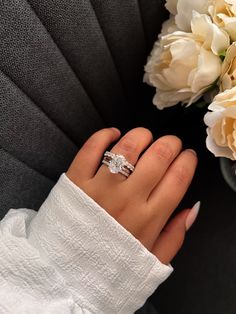 a close up of a person's hand with a ring and flowers in the background