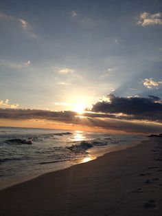 the sun is setting over the ocean with footprints in the sand and on the beach