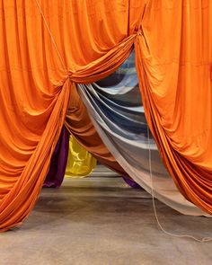 an orange drape is hanging from the ceiling in front of several different colored curtains