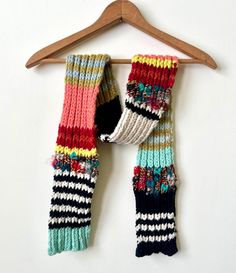 two multicolored knitted scarfs hanging on a wooden hanger