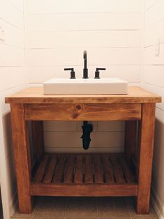 a bathroom sink sitting under a wooden shelf next to a white tiled wall and floor