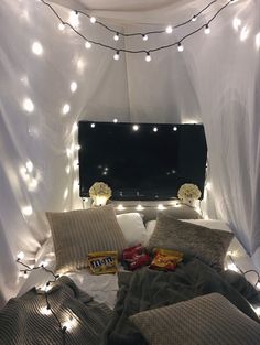 a bed that has some lights on the headboard and pillows in front of it