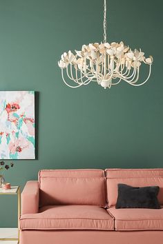 a living room with a pink couch and chandelier hanging from the ceiling in front of a green wall