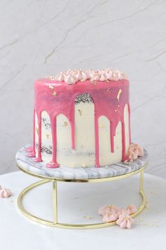 a cake with pink icing and white frosting on a gold stand next to flowers