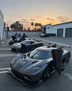 three black sports cars parked in a parking lot at sunset with palm trees behind them