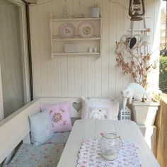 a white table topped with lots of pillows next to a shelf filled with plates and bowls