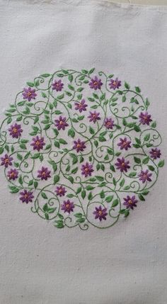 a white cloth with purple flowers and green leaves in the center is embroidered onto it