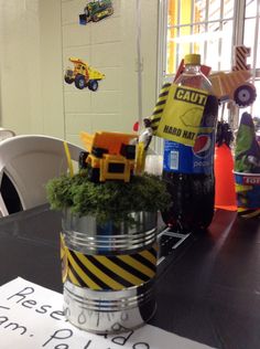 a table topped with a bucket filled with green plants and construction vehicles next to a sign that says caution