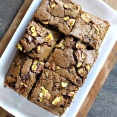 some brownies are on a white plate with walnuts and other nuts around them