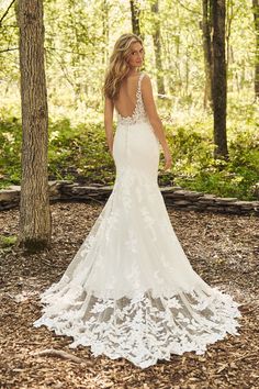 a woman in a white wedding dress standing in the woods with her back to the camera