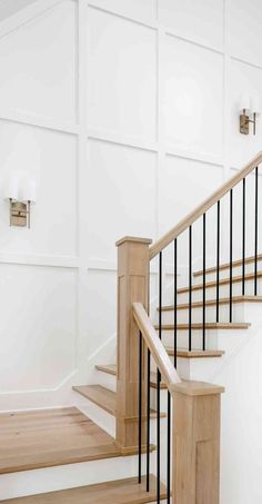 an empty room with white walls and wooden stairs in front of a wall mounted light fixture