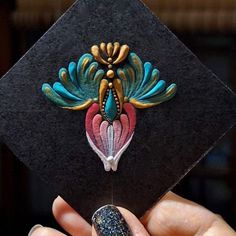 a hand holding a black and gold graduation cap with colorful designs on the front end