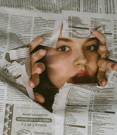 a woman looking through torn newspaper with her hands