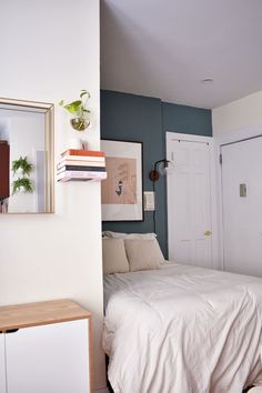 a white bed sitting next to a wooden dresser under a painting on the wall in a bedroom