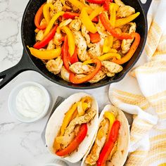 chicken fajitas with peppers and onions in a cast iron skillet on a marble countertop