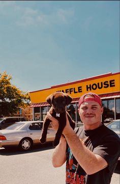 a man holding up a stuffed animal in front of a fire house store with cars parked behind him