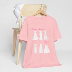 This t shirt is a must-have for any bride or bridesmaid who loves wedding dresses. It features a chic design of elegant outlines of dresses in different styles. It's a perfect way to express your style and your excitement for the big day.  You can wear this t shirt for any pre-wedding event, such as wedding dress shopping, bridal showers, hen parties, or just hanging out with the bride squad. It's also a wonderful gift idea for the bride or her besties.  This t shirt is made from soft and comfor White Bridal T-shirt With Short Sleeves, Summer Short Sleeve T-shirt For Bridal Shower, Summer Bridal Shower Short Sleeve T-shirt, Short Sleeve Tops For Bridesmaids, White T-shirt For Bridal Shower Short Sleeve, White Short Sleeve T-shirt For Bridal Shower, White Short Sleeve Bride T-shirt, Bride's White Short Sleeve T-shirt, White Short Sleeve Top For Bridesmaids