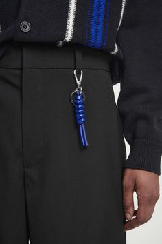 a man in black pants with a blue keychain on his lapel is shown from the waist up