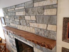 a stone fireplace in a living room with wood mantle