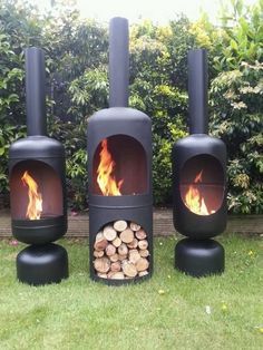 three black outdoor fireplaces with firewood stacked in front of them on the grass