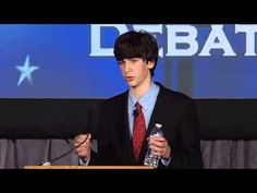 a man in a suit and tie giving a speech at a podium with a bottle of water